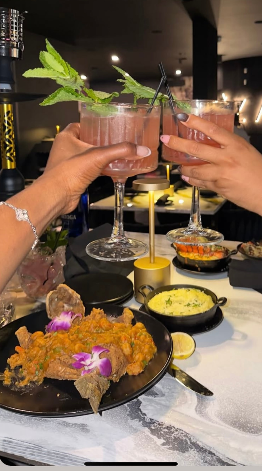 Two guests toasting pink cocktails over dinner at Aziza